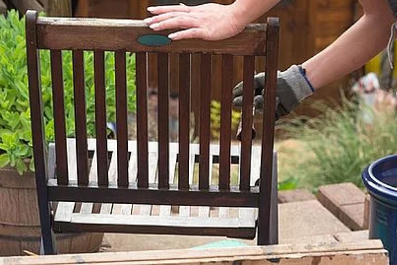 Person streicht Gartenstuhl mit Pinsel